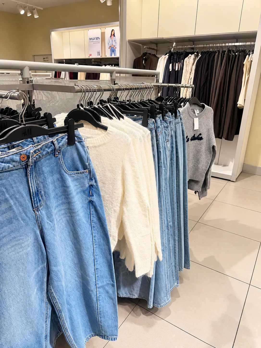 ג׳ינס וסריגים בהירים על מתלה בחנות H&M