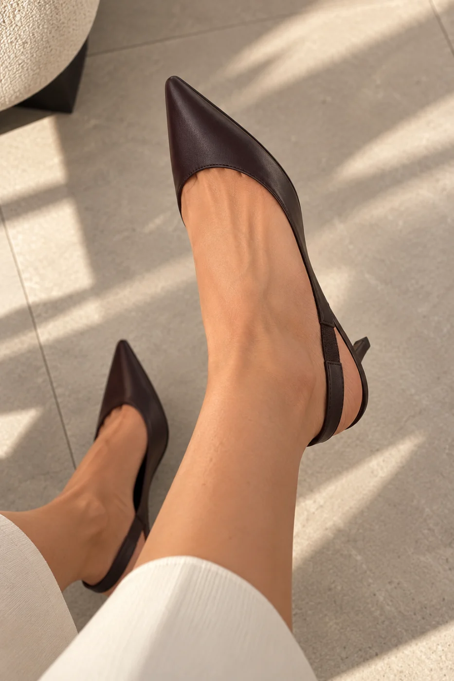 Dark brown leather slingback pumps with a pointed toe, worn with cream ribbed trousers