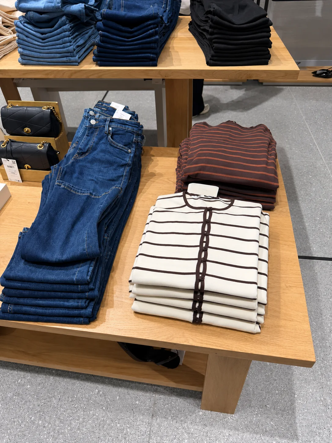Folded jeans beside striped and burgundy knits on a wooden display table