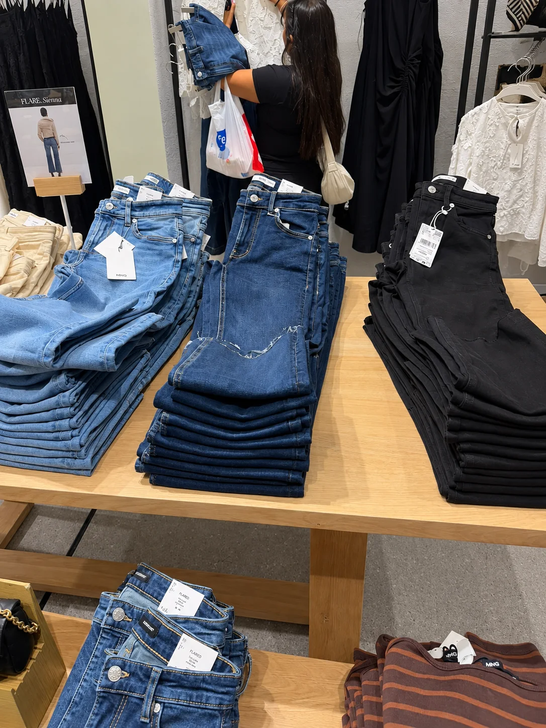 Stacks of folded jeans on wooden tables in a Mango store denim area