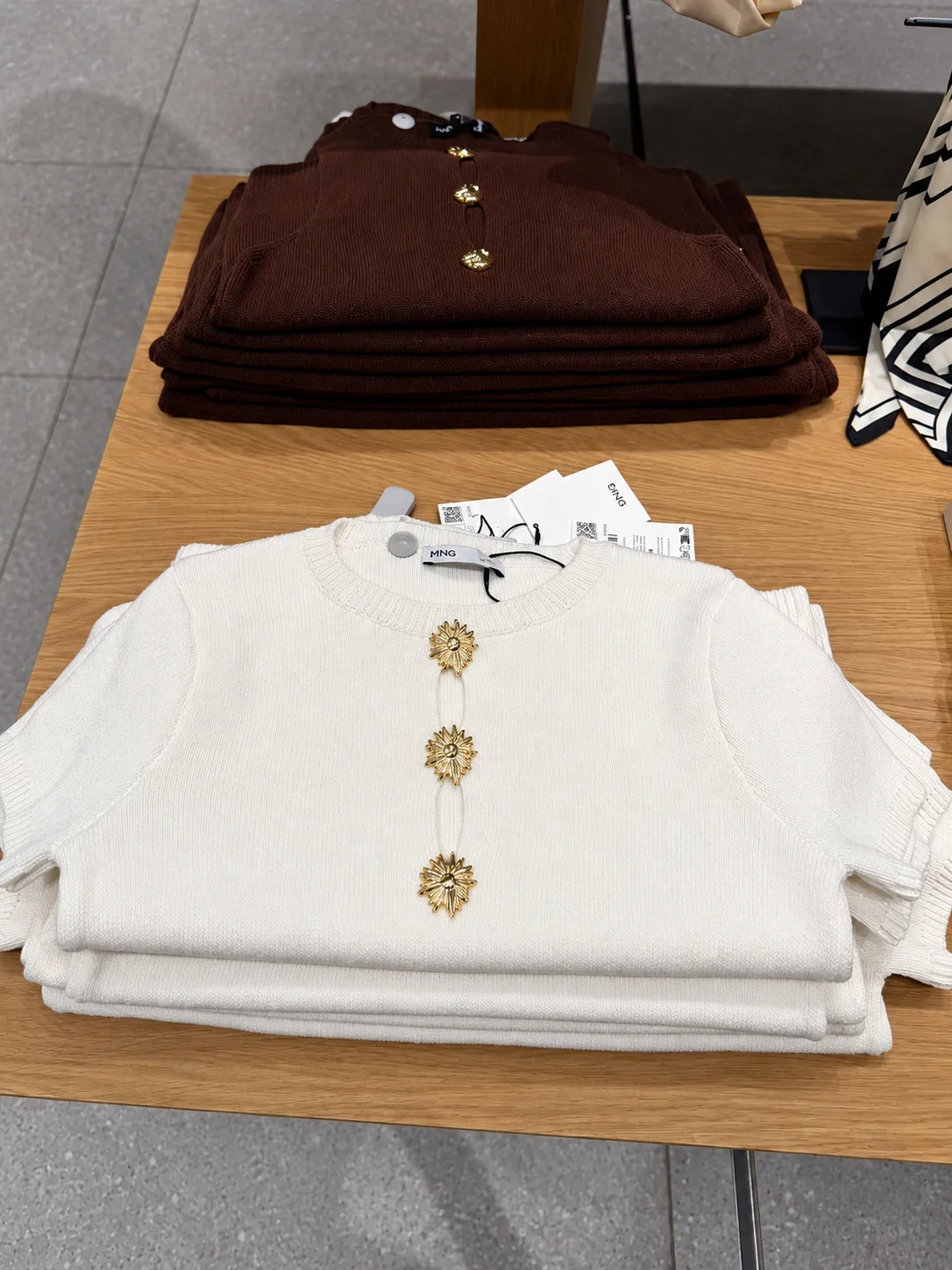 Folded burgundy and cream knits with gold buttons on a wooden store table