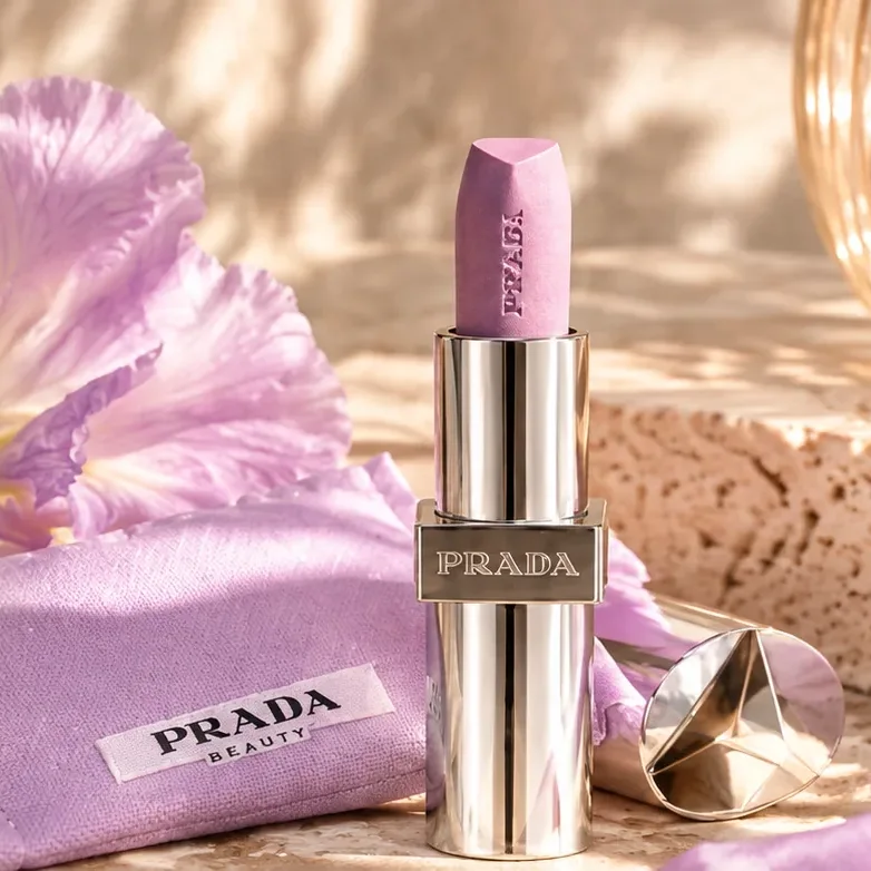 Prada Balm Luminizing Care בגוון לילך לצד הנרתיק של Prada Beauty על מדף אבן מואר בשמש