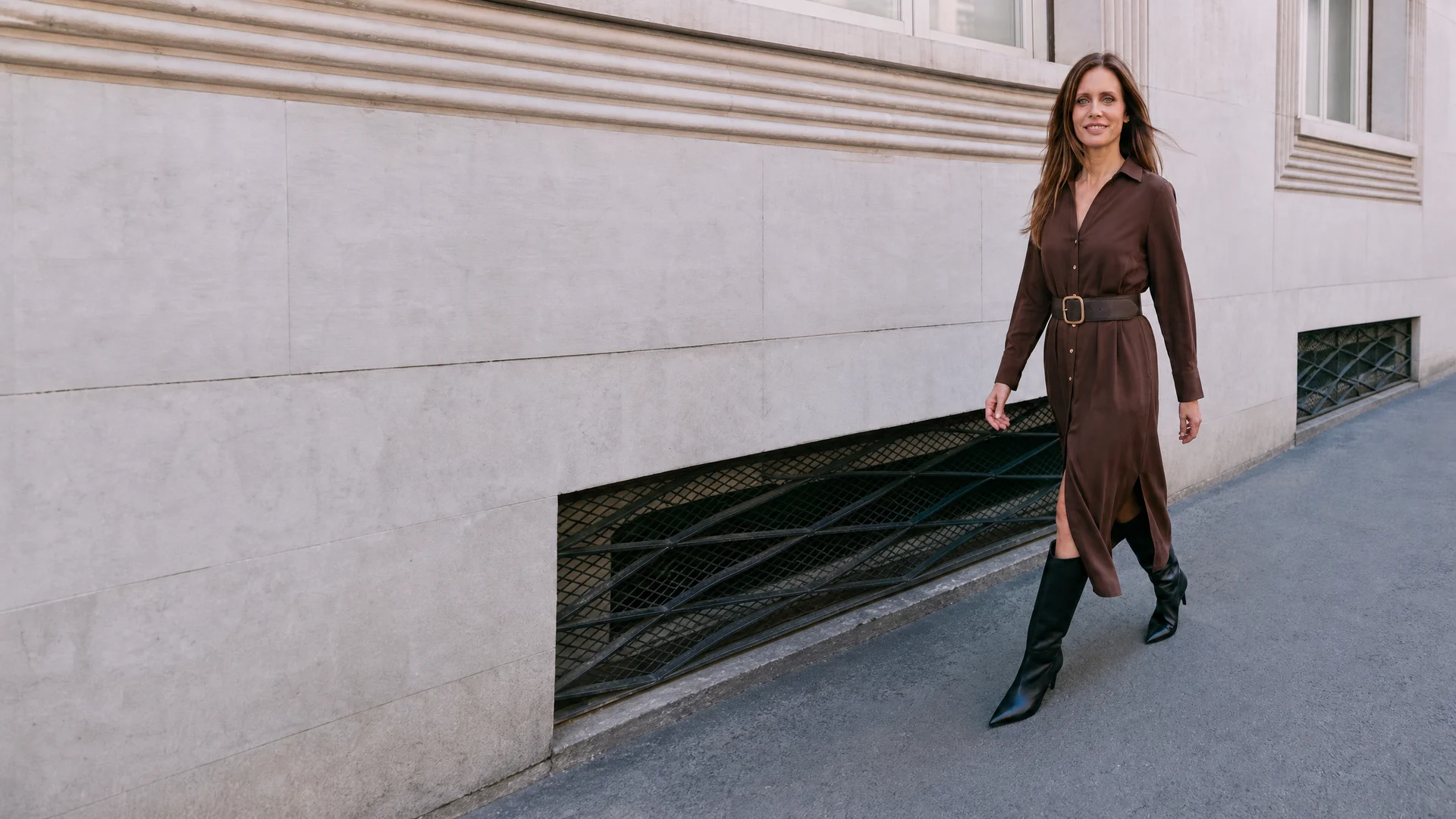 Michelle Loren walking down the street in a brown belted shirt dress and black knee boots